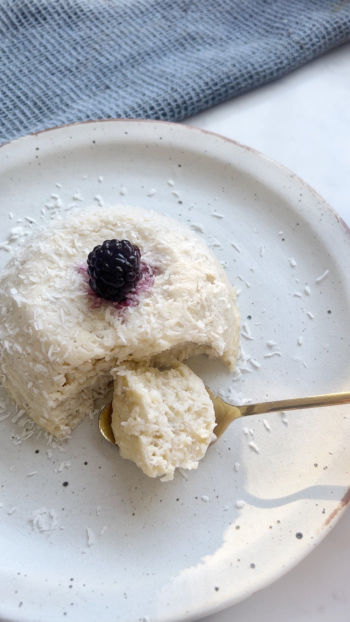 Flourless coconut cake in a ramekin topped with fresh berries and coconut flakes, served on a rustic plate.