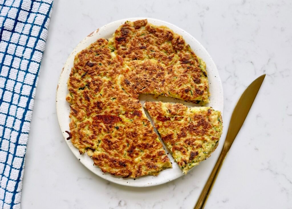 Golden-brown Zucchini Skillet Cake with crispy edges, sliced into wedges, garnished with herbs and served on a plate.