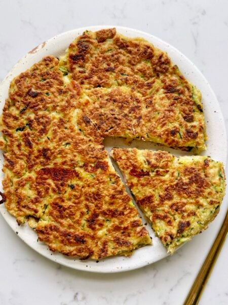 Golden-brown Zucchini Skillet Cake with crispy edges, sliced into wedges, garnished with herbs and served on a plate.