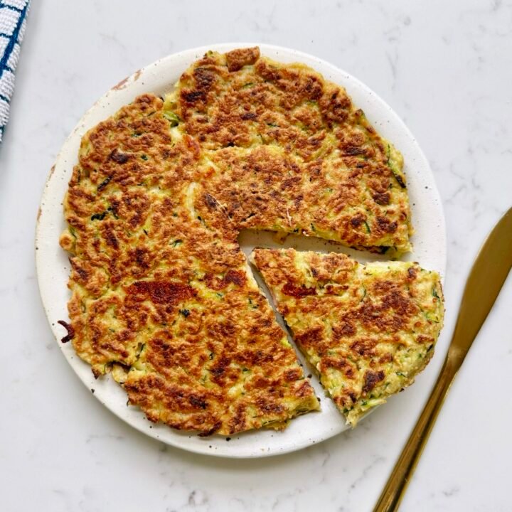 Golden-brown Zucchini Skillet Cake with crispy edges, sliced into wedges, garnished with herbs and served on a plate.