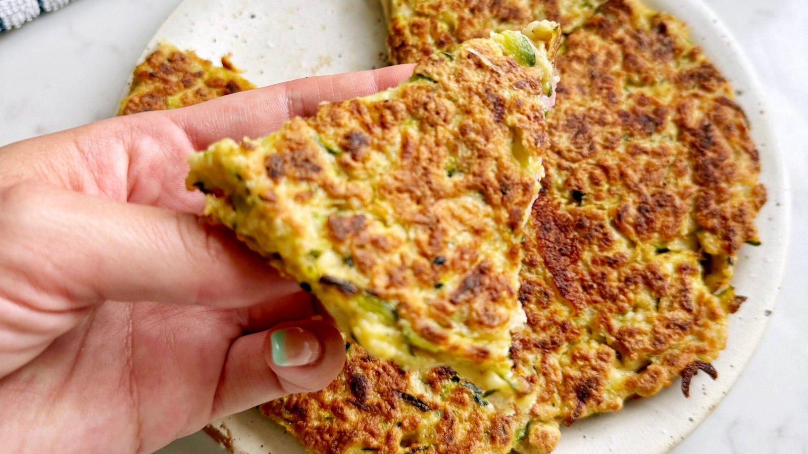 "Golden-brown Zucchini Skillet Cake with crispy edges, sliced into wedges, garnished with herbs and served on a plate