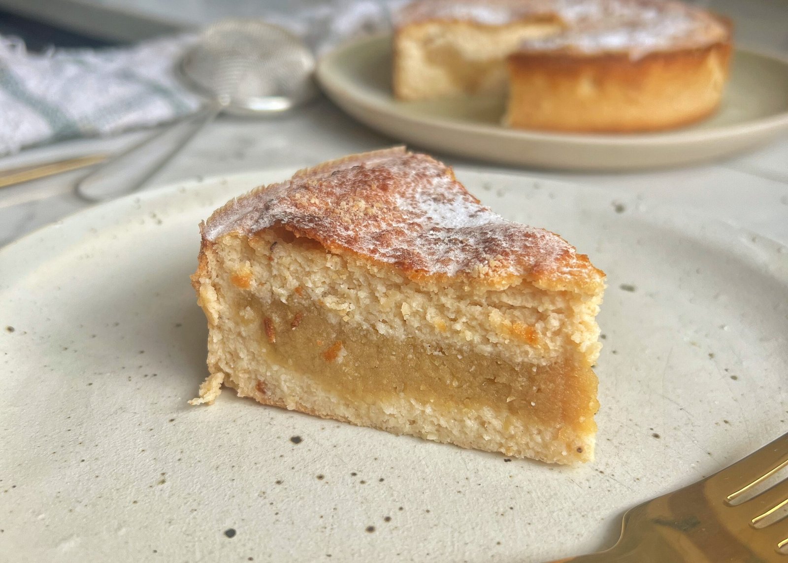 A freshly baked Apple and Almond Yoghurt Cake with a golden-brown crust, sliced to reveal a soft, moist interior with a layer of apple purée in the middle. The cake is presented on a wooden board, garnished with a sprinkle of cinnamon and slivered almonds, with a dollop of yoghurt on the side." Let me know if you'd like any adjustments! 