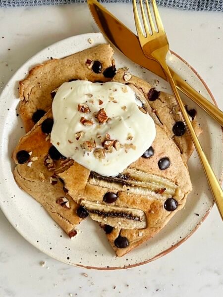 "Deliciosos Banana Bread Sheet Pan Pancakes horneados en una bandeja, cortados en porciones y decorados con rodajas de plátano y chispas de chocolate