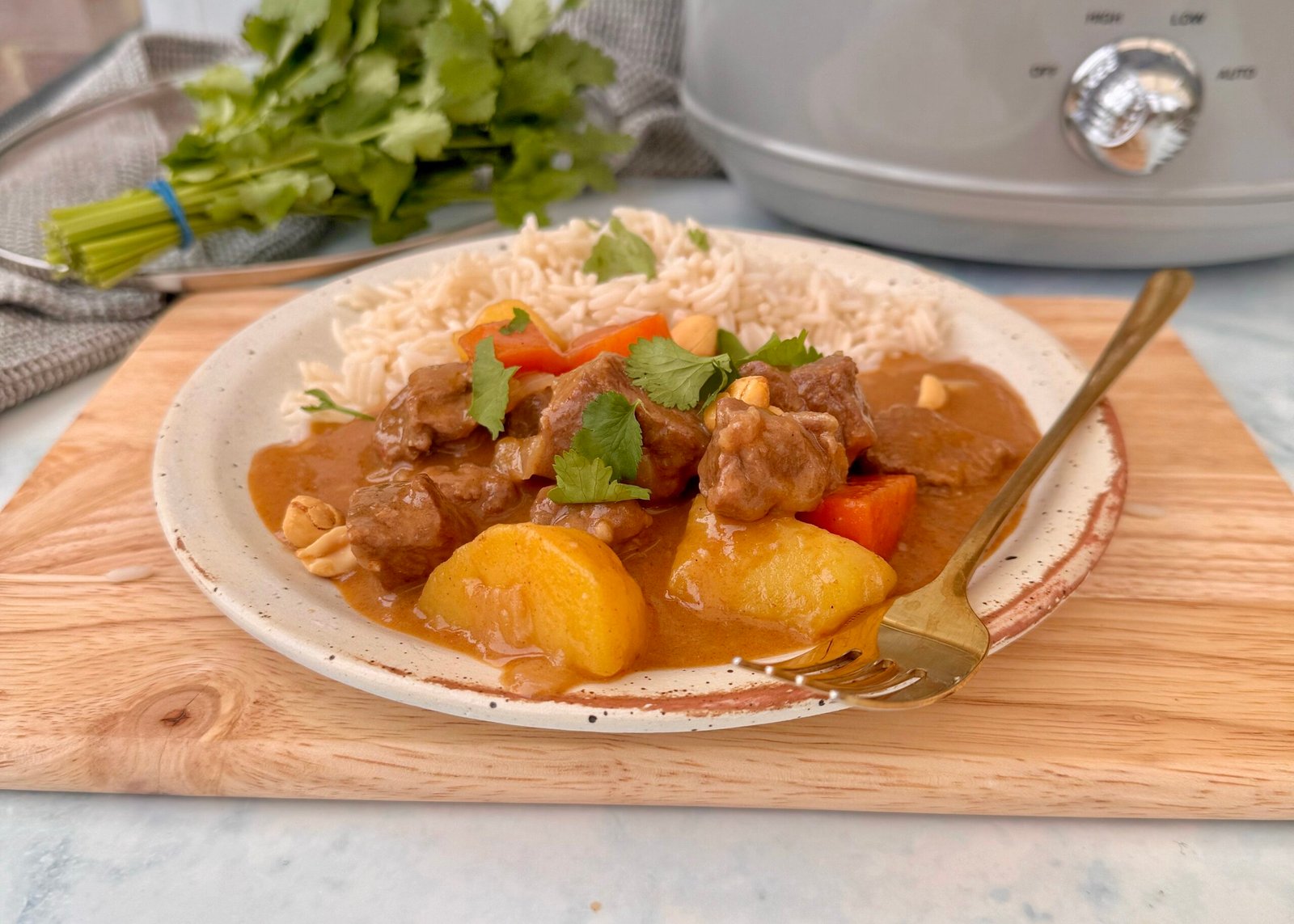 A bowl of steaming Beef Massaman Curry featuring tender beef chunks, diced potatoes, and carrots in a creamy, spiced coconut milk sauce, garnished with fresh coriander and served over jasmine rice.
