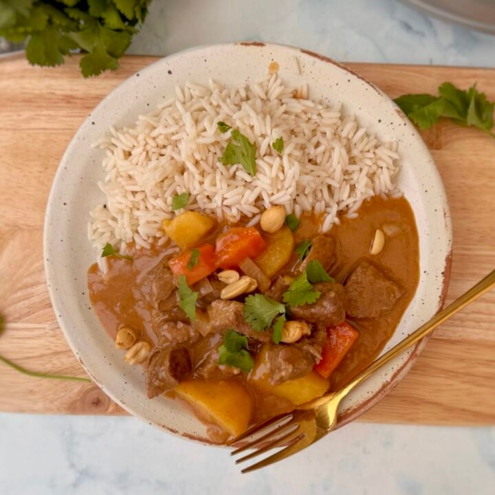 A bowl of steaming Beef Massaman Curry featuring tender beef chunks, diced potatoes, and carrots in a creamy, spiced coconut milk sauce, garnished with fresh coriander and served over jasmine rice.