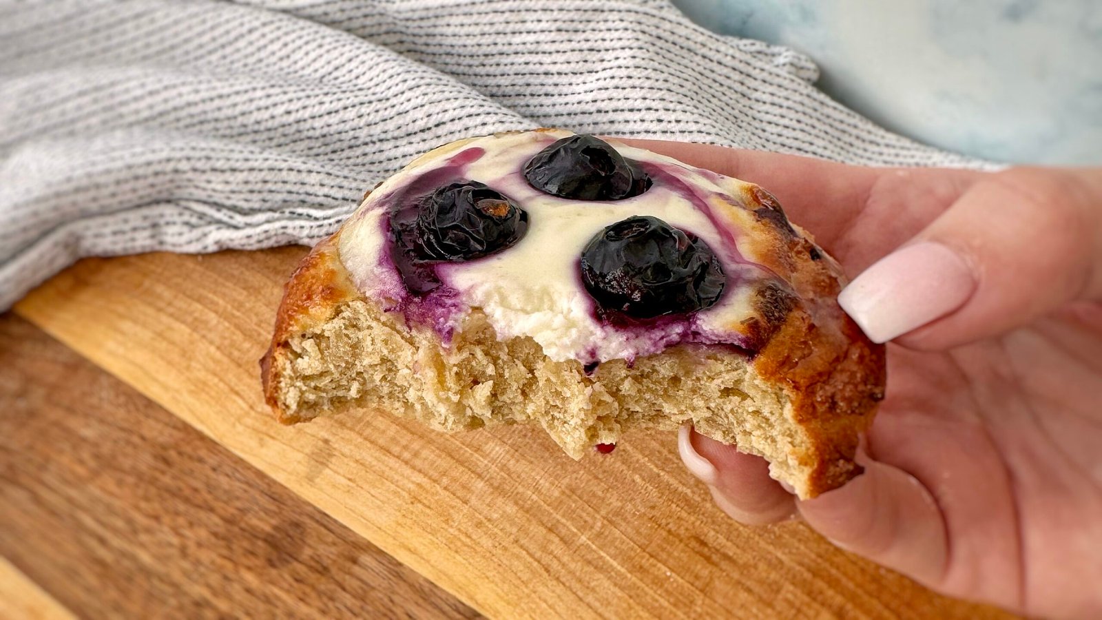 A close-up of freshly baked Blueberry Breakfast Buns with a golden-brown exterior, filled with creamy yoghurt and juicy blueberries. The buns are placed on a white plate, with a drizzle of sugar-free maple syrup and a sprinkle of fresh berries around them. The soft, fluffy texture contrasts with the vibrant blueberries, making for a delicious and healthy breakfast treat.