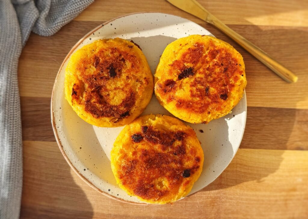 Crispy, golden-brown cheese-stuffed plantain arepas with a soft, sweet interior and gooey melted cheese filling, served warm on a plate with avocado slices and a side of dipping sauce.