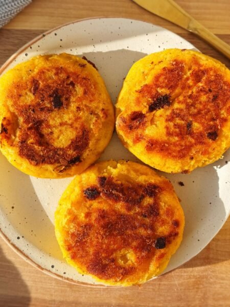 Crispy, golden-brown cheese-stuffed plantain arepas with a soft, sweet interior and gooey melted cheese filling, served warm on a plate with avocado slices and a side of dipping sauce.