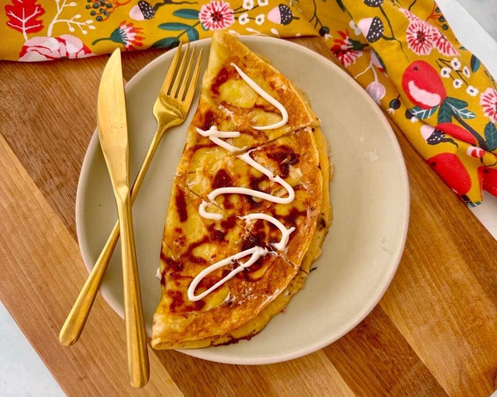 A golden, crispy Cheesy Potato Omelette in a skillet, featuring thinly sliced potatoes, melted cheese, and fluffy eggs, garnished with fresh herbs.