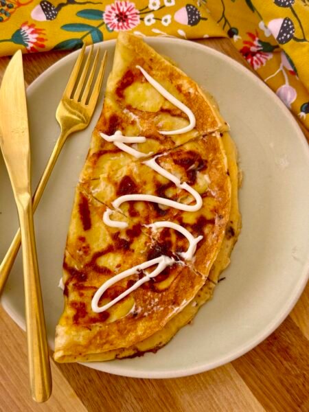 A golden, crispy Cheesy Potato Omelette in a skillet, featuring thinly sliced potatoes, melted cheese, and fluffy eggs, garnished with fresh herbs.