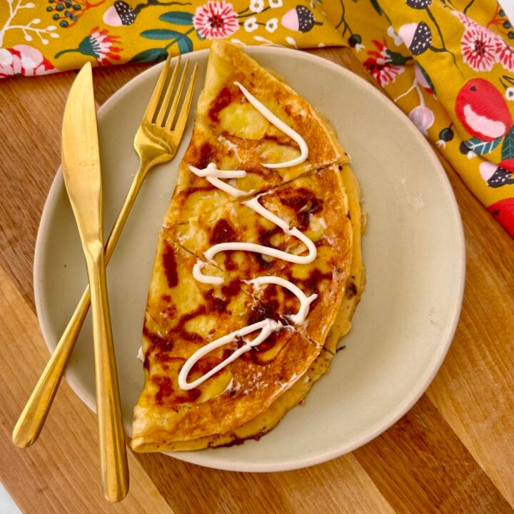 A golden, crispy Cheesy Potato Omelette in a skillet, featuring thinly sliced potatoes, melted cheese, and fluffy eggs, garnished with fresh herbs.