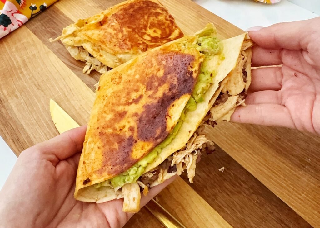 Chipotle Chicken Folded Wraps with a crispy golden-brown tortilla, filled with smoky chipotle chicken, melted cheddar cheese, creamy avocado, and spiced kidney beans, served on a wooden board with a side of fresh greens and lime wedges.