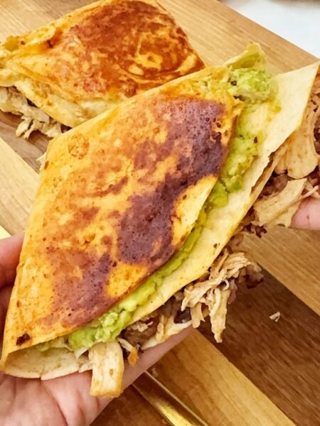 Chipotle Chicken Folded Wraps with a crispy golden-brown tortilla, filled with smoky chipotle chicken, melted cheddar cheese, creamy avocado, and spiced kidney beans, served on a wooden board with a side of fresh greens and lime wedges.