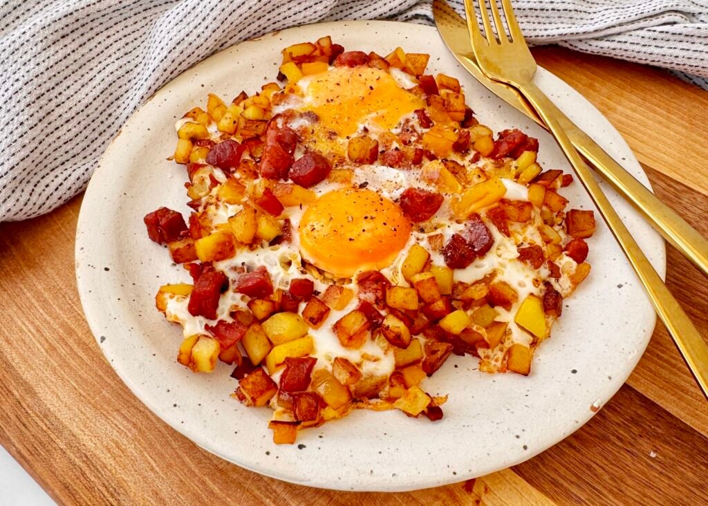 A hearty and flavorful Chorizo Egg Hash served in a skillet. Crispy golden-brown potatoes, smoky chorizo, and perfectly cooked eggs with runny yolks are garnished with paprika and fresh herbs. The dish is vibrant with yellow bell peppers and caramelized onions, making it a delicious and satisfying one-pan meal.