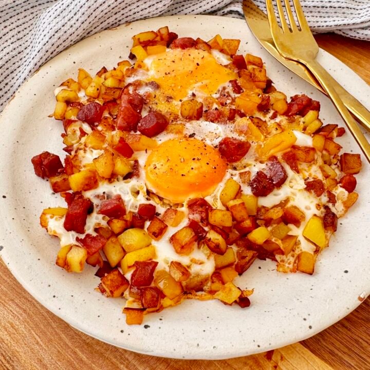 A hearty and flavorful Chorizo Egg Hash served in a skillet. Crispy golden-brown potatoes, smoky chorizo, and perfectly cooked eggs with runny yolks are garnished with paprika and fresh herbs. The dish is vibrant with yellow bell peppers and caramelized onions, making it a delicious and satisfying one-pan meal.