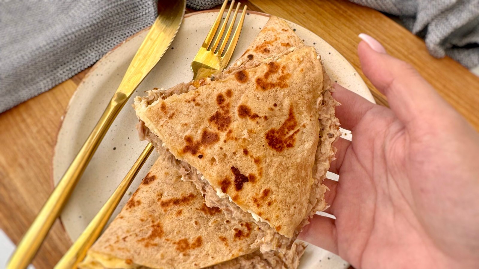 A golden-brown tortilla omelette folded in half, filled with creamy cottage cheese and a savory tuna mixture. The omelette sits on a plate, garnished with fresh herbs, with a side of salad and a drizzle of hot sauce for extra flavor.
