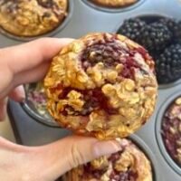 Freshly baked blackberry coconut oatmeal muffins on a cooling rack, with juicy blackberries and shredded coconut sprinkled around.