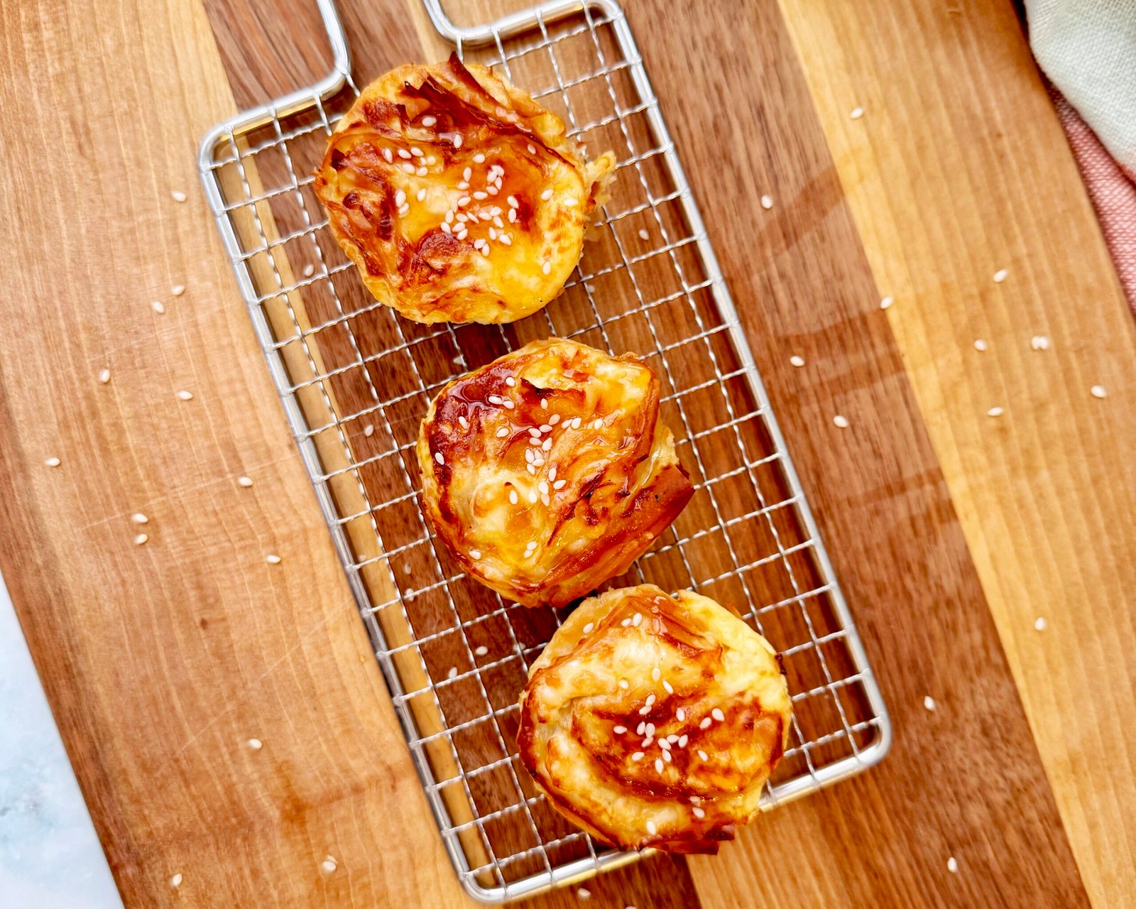 A golden, crispy filo pastry nest filled with creamy feta custard, drizzled with glistening hot honey. The delicate, crinkled layers of pastry create a light, airy texture, topped with sesame seeds for an extra crunch. Served in a muffin tin or on a rustic wooden board, these mini crinkle pies are an irresistible blend of sweet and savoury, perfect for appetizers or brunch.