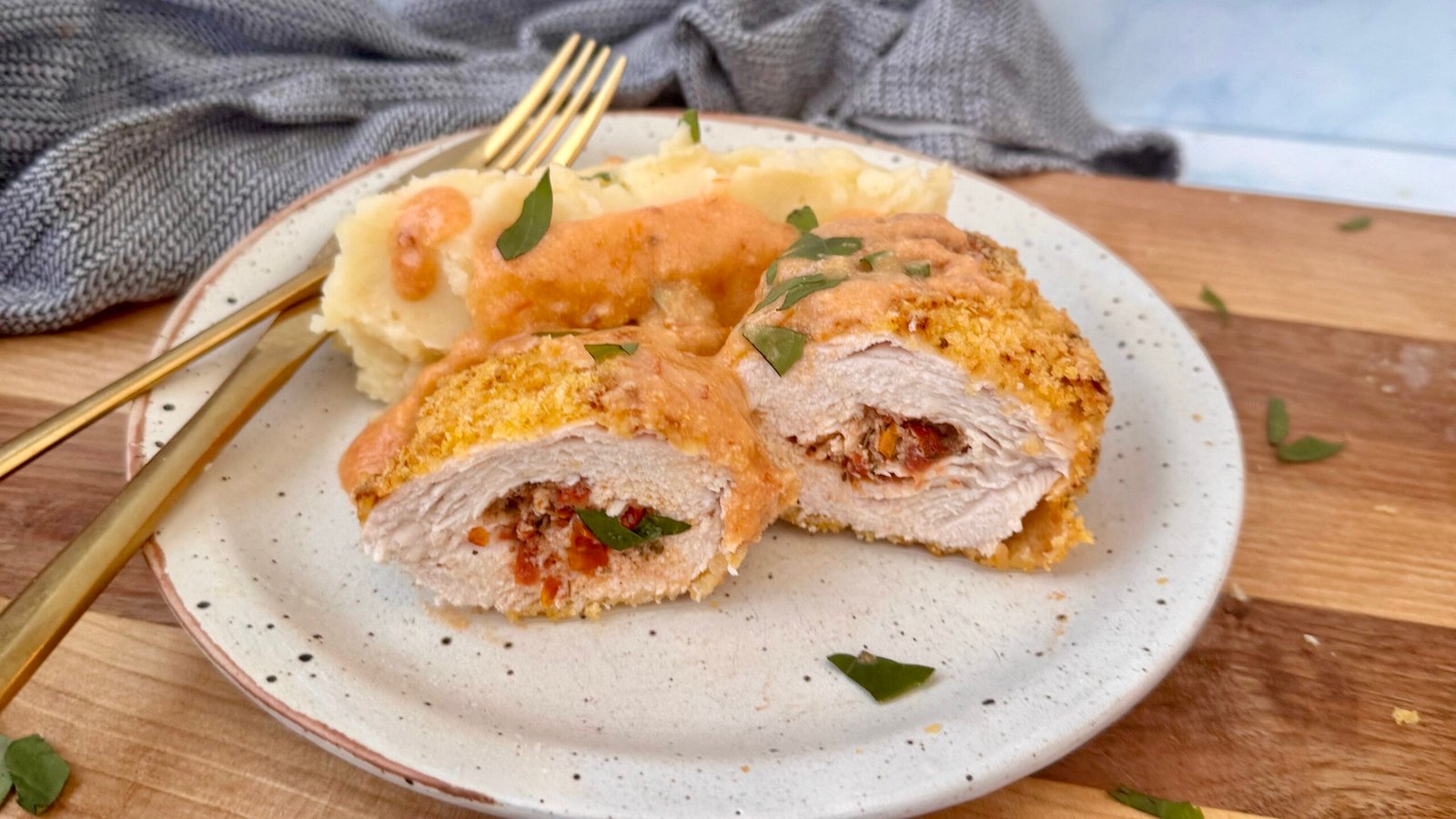 Golden, crispy Marry Me Chicken Kiev sliced open to reveal a rich sun-dried tomato and Parmesan filling, served with creamy mashed potatoes and a drizzle of cottage cheese sauce, garnished with fresh basil.