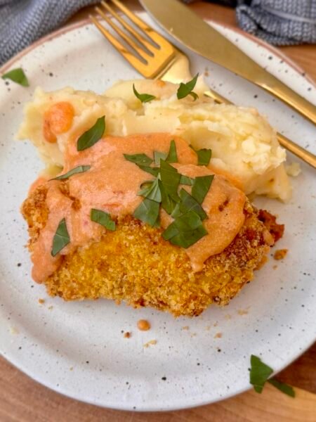 Golden, crispy Marry Me Chicken Kiev sliced open to reveal a rich sun-dried tomato and Parmesan filling, served with creamy mashed potatoes and a drizzle of cottage cheese sauce, garnished with fresh basil.