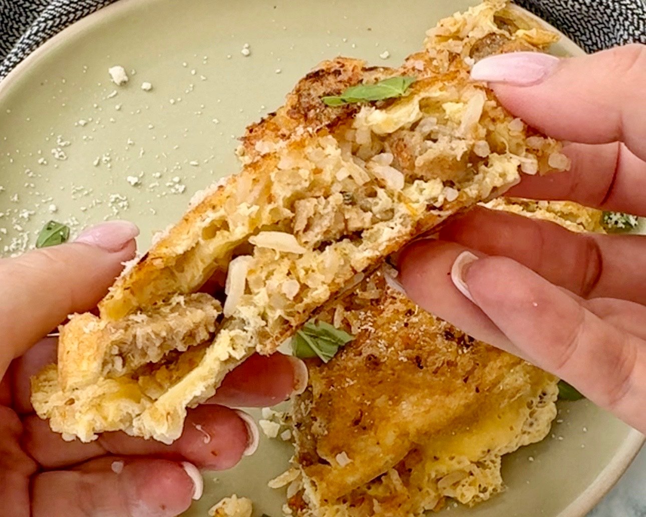 A golden-brown omelette folded over a flavorful filling of pesto-infused rice and vegetarian sausage, garnished with freshly grated Parmesan cheese. Served on a white plate with a side of fresh greens.