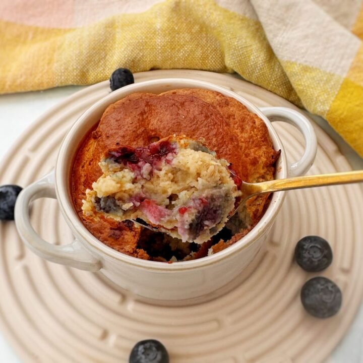 A golden-baked oatmeal dish studded with blueberries, served warm in a small white ramekin with a spoon on the side