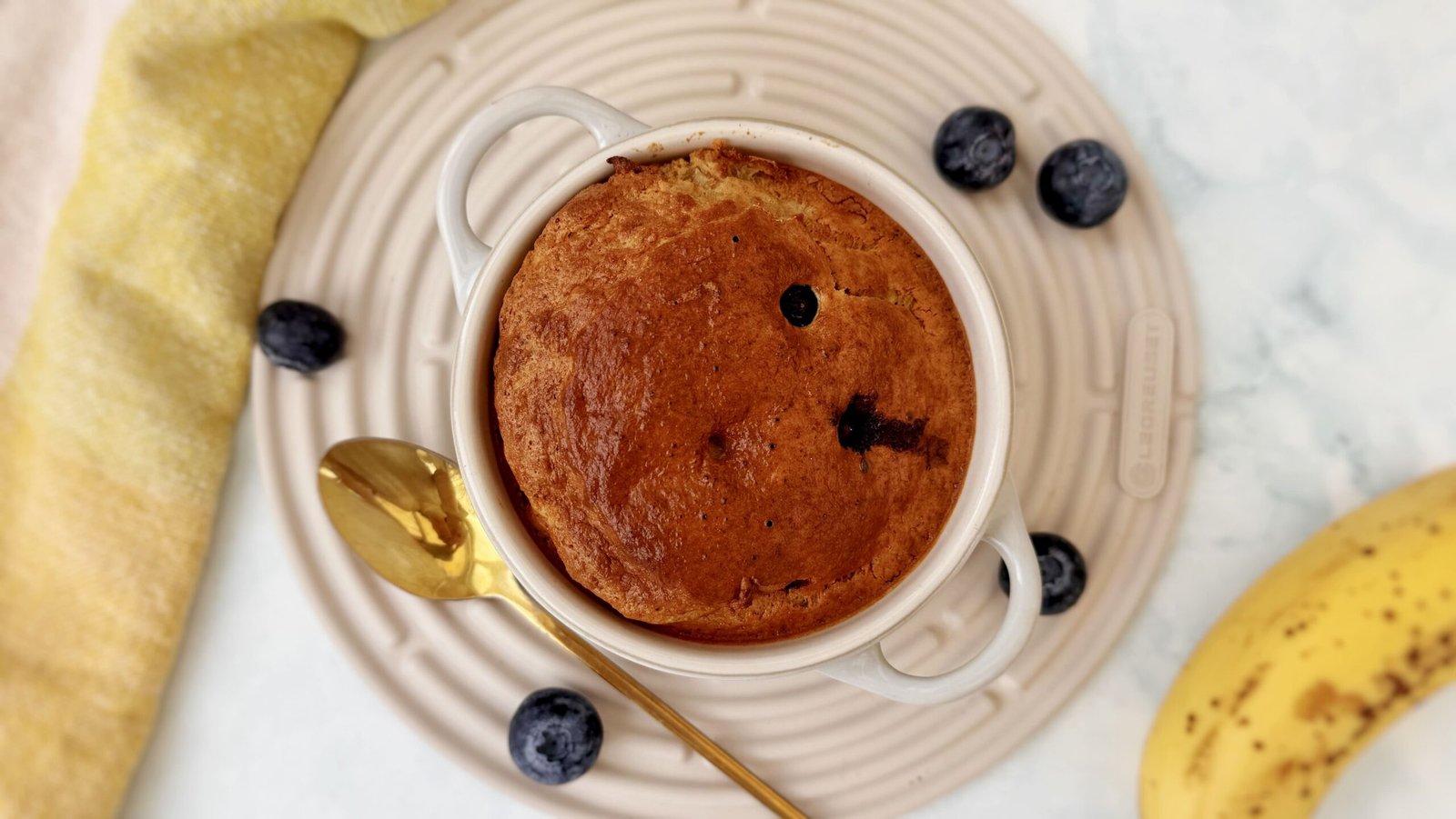 A golden-baked oatmeal dish studded with blueberries, served warm in a small white ramekin with a spoon on the side