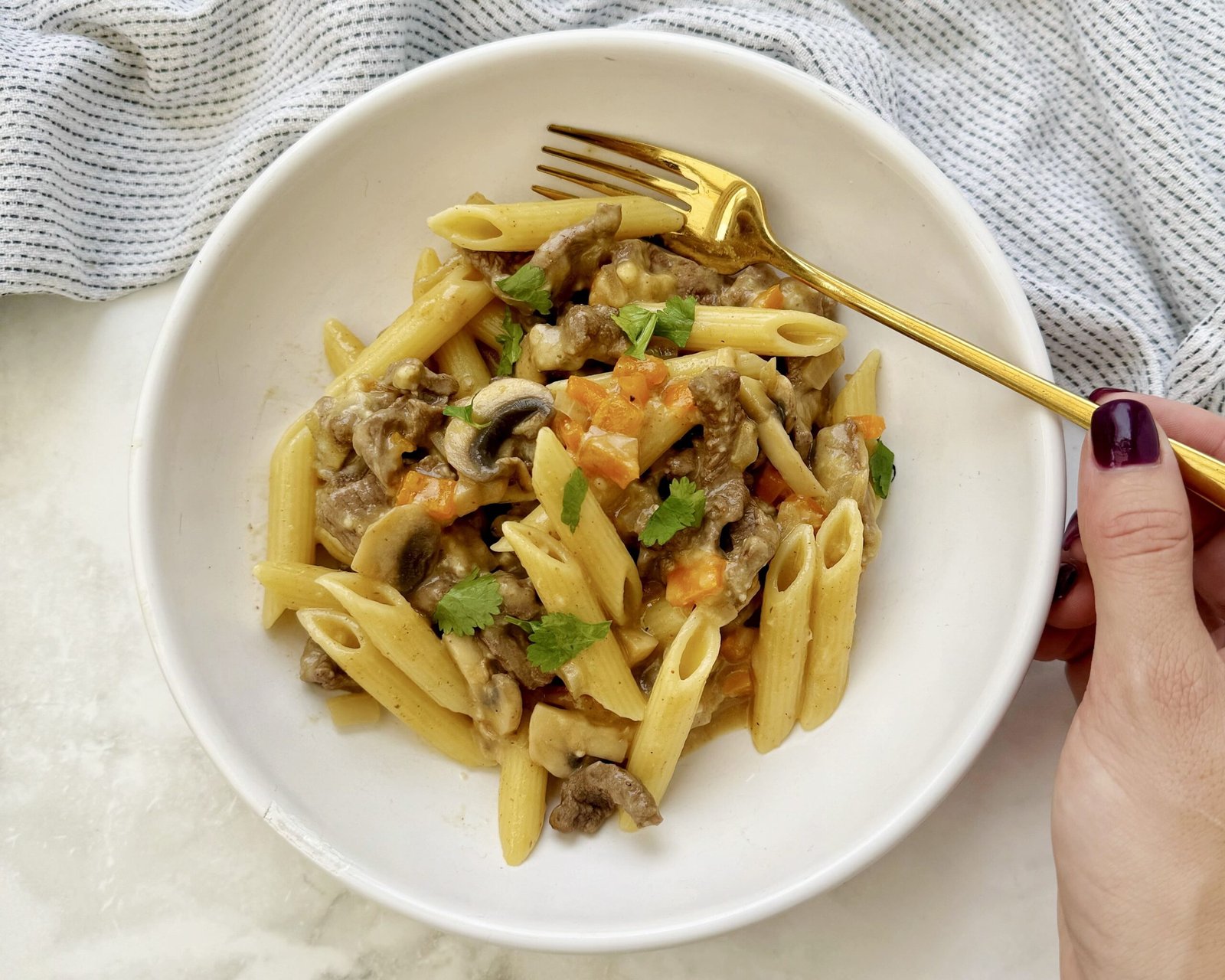 A hearty plate of cheesesteak pasta featuring thin slices of seared beef, colorful sautéed peppers, mushrooms, and onions, all tossed with whole wheat pasta in a creamy, cheesy sauce.