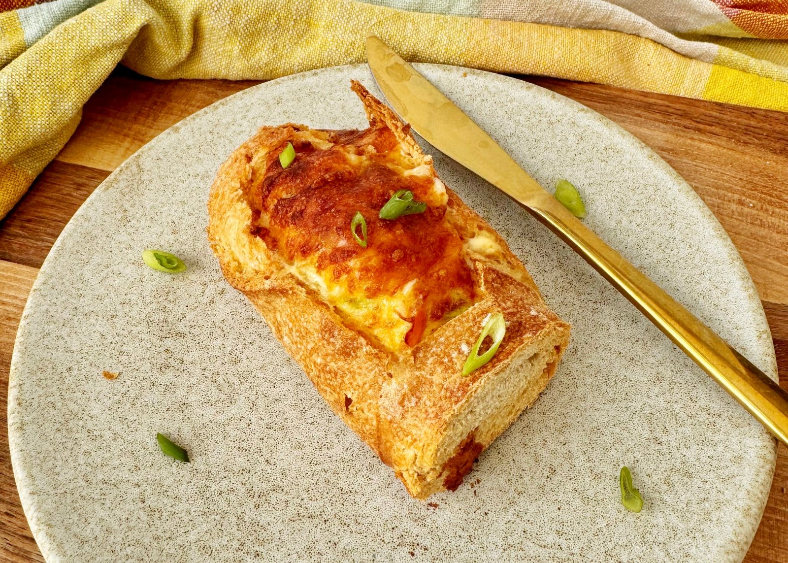 Cheesy Egg Baguette Bake sliced open to reveal a creamy egg filling with peppers and spring onions, topped with melted golden cheese, served on a rustic wooden board.