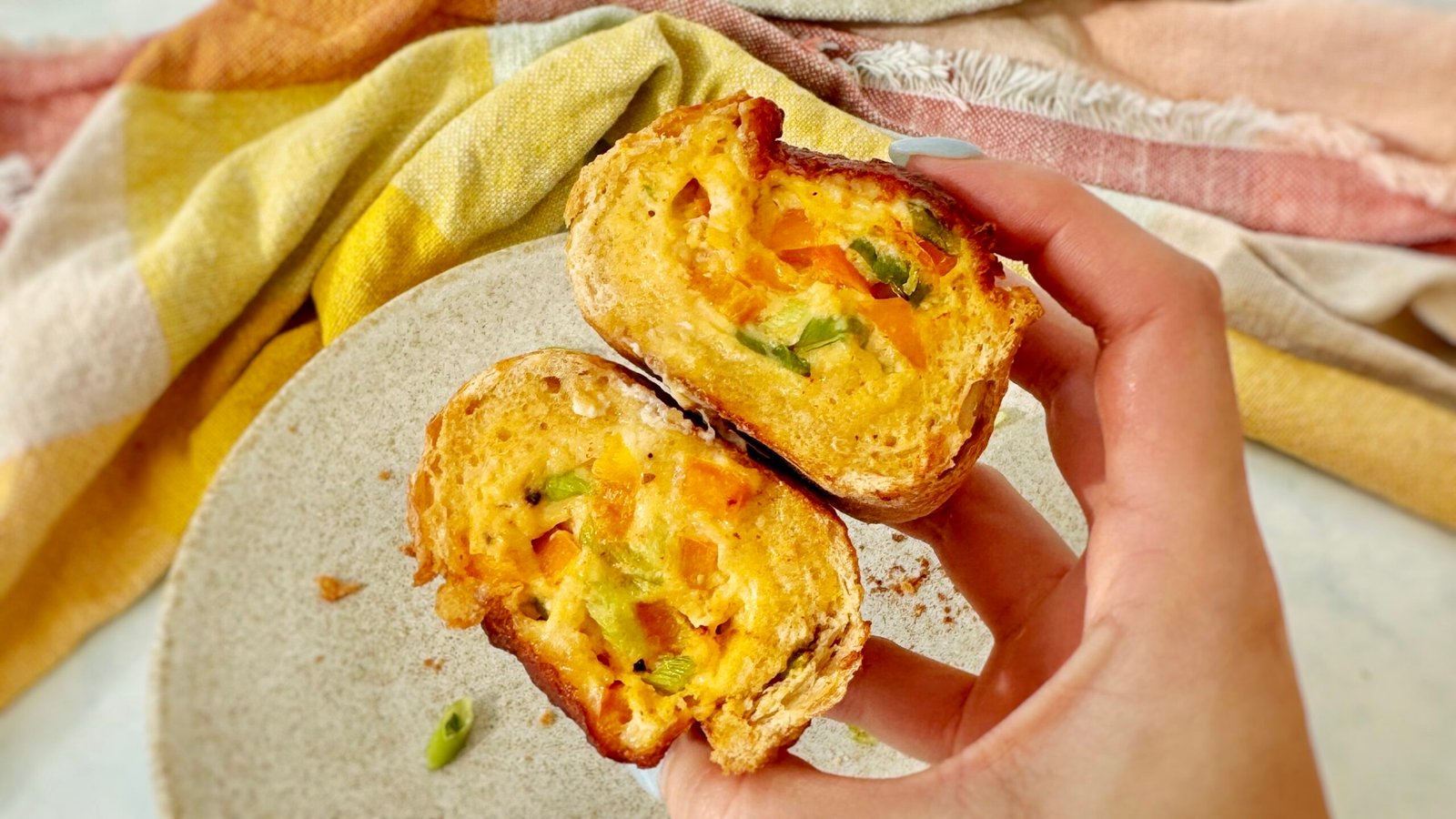 Cheesy Egg Baguette Bake sliced open to reveal a creamy egg filling with peppers and spring onions, topped with melted golden cheese, served on a rustic wooden board.