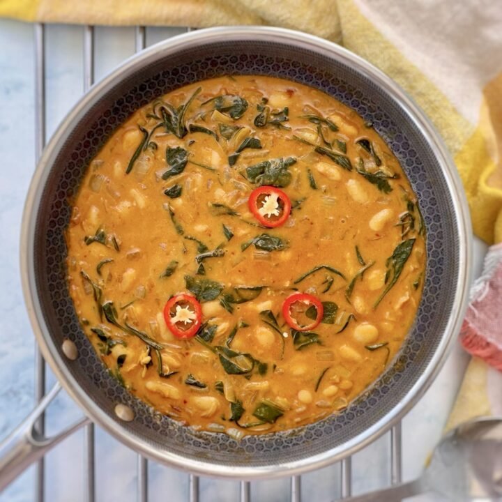 Bowl of creamy butter beans in coconut sauce garnished with spinach and herbs