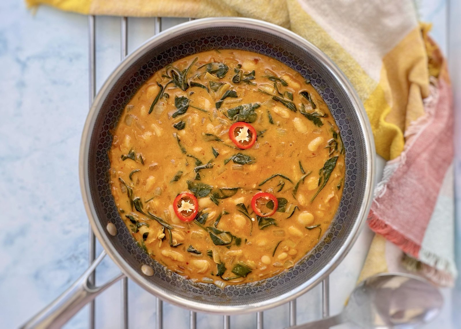 Bowl of creamy butter beans in coconut sauce garnished with spinach and herbs