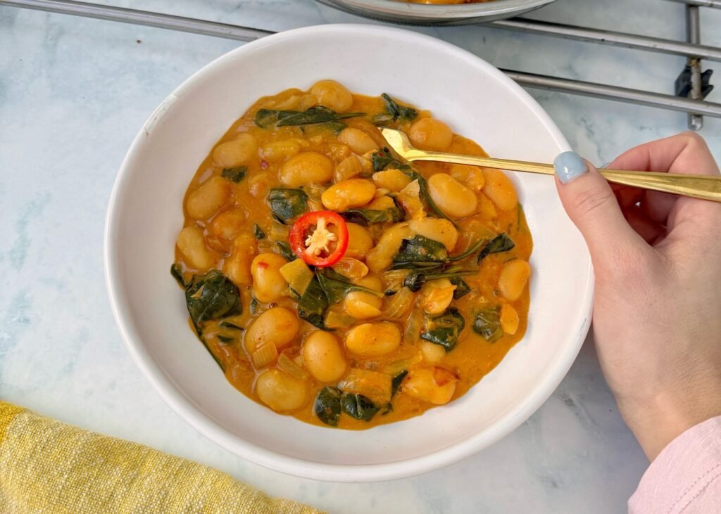 Bowl of creamy butter beans in coconut sauce garnished with spinach and herbs