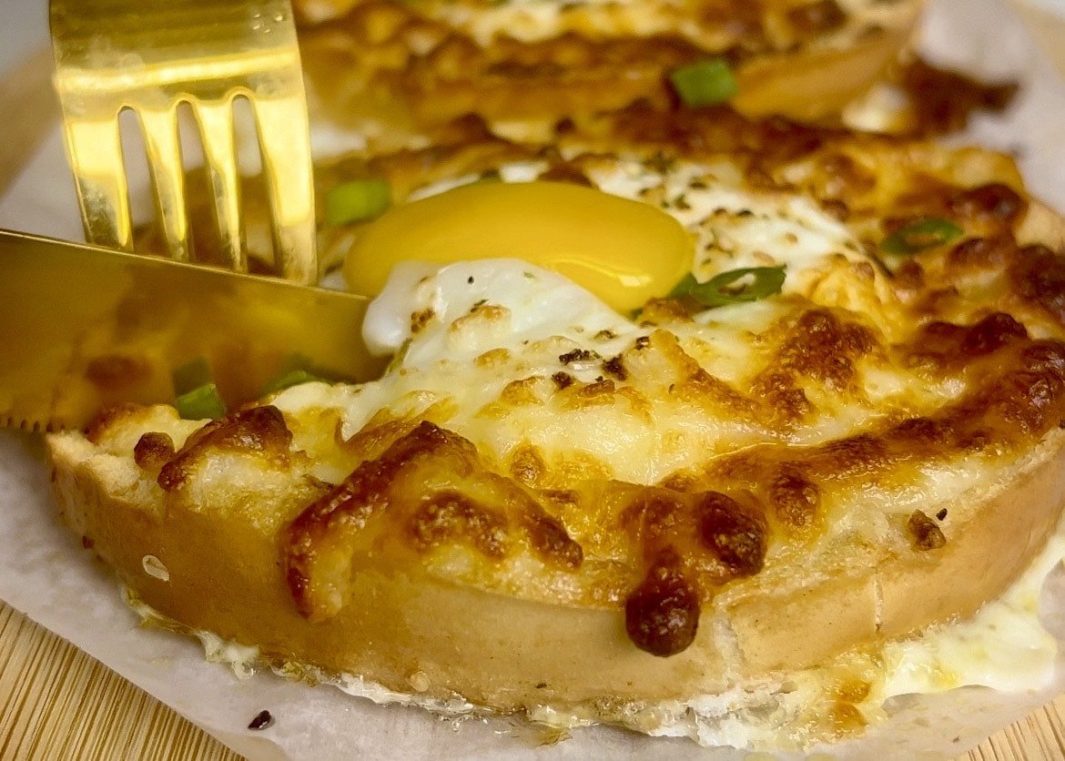 Air fryer egg bagels with melted cheese and sunny side eggs on a wooden plate.