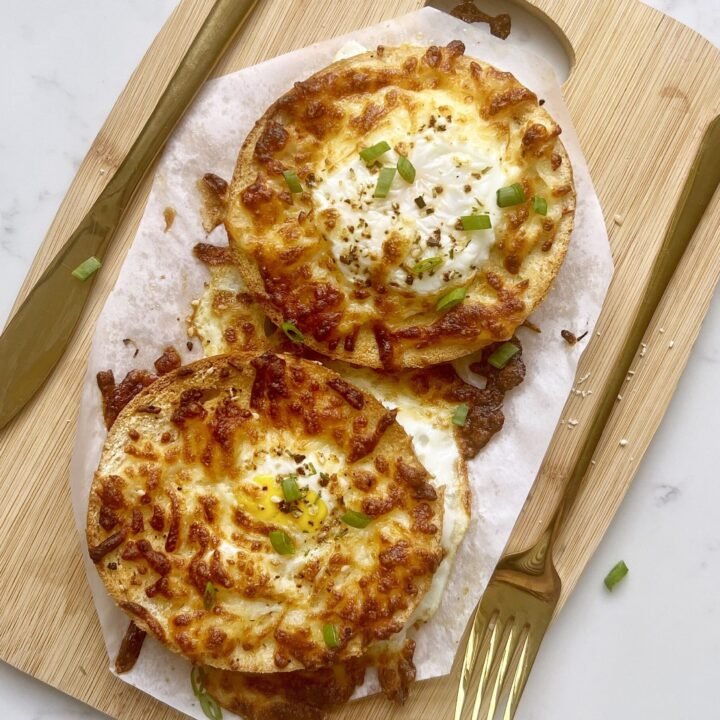 Air fryer egg bagels with melted cheese and sunny side eggs on a wooden plate.