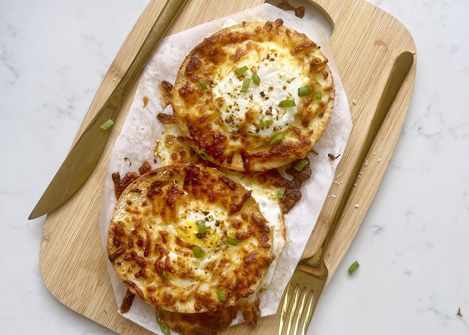 Air fryer egg bagels with melted cheese and sunny side eggs on a wooden plate.