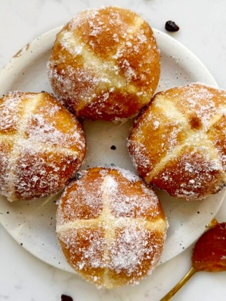 Golden-brown hot cross bun doughnuts with orange marmalade glaze and white crosses, coated lightly in erythritol, served on a wire rack