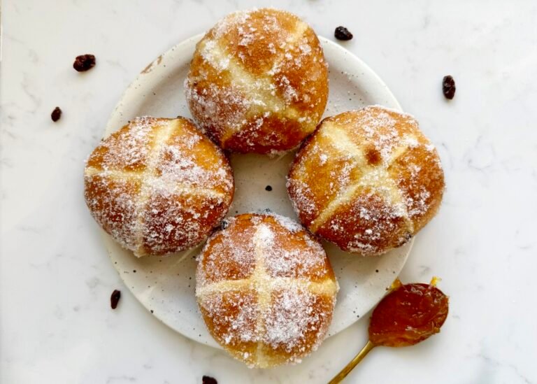 Golden-brown hot cross bun doughnuts with orange marmalade glaze and white crosses, coated lightly in erythritol, served on a wire rack