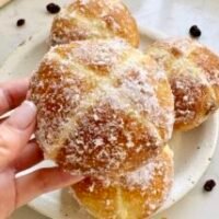 Golden-brown hot cross bun doughnuts with orange marmalade glaze and white crosses, coated lightly in erythritol, served on a wire rack