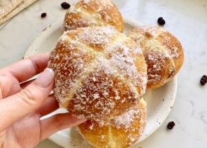 Golden-brown hot cross bun doughnuts with orange marmalade glaze and white crosses, coated lightly in erythritol, served on a wire rack