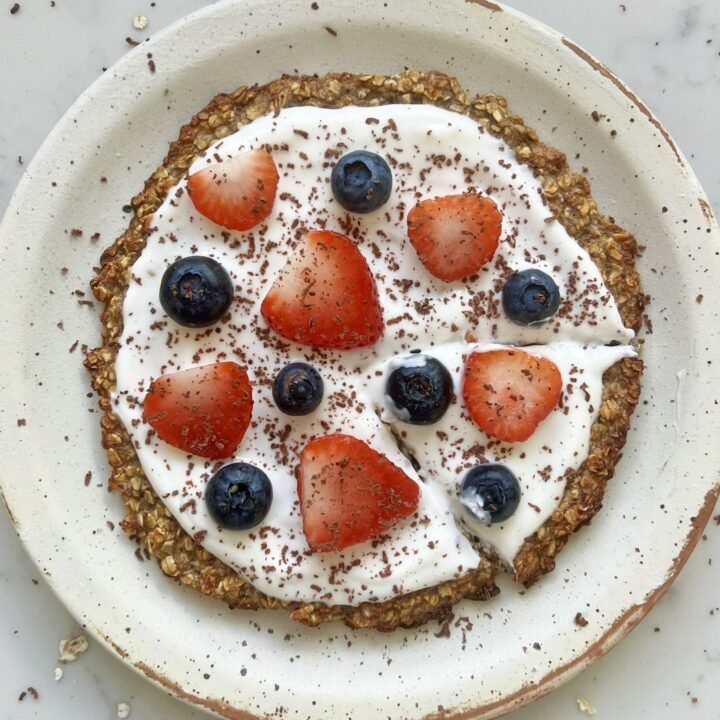 Healthy oatmeal breakfast pizza topped with yoghurt, strawberries, blueberries, and dark chocolate shavings.