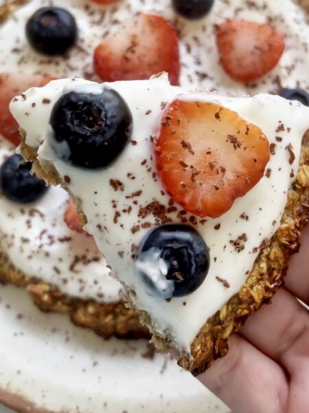 Healthy oatmeal breakfast pizza topped with yoghurt, strawberries, blueberries, and dark chocolate shavings.