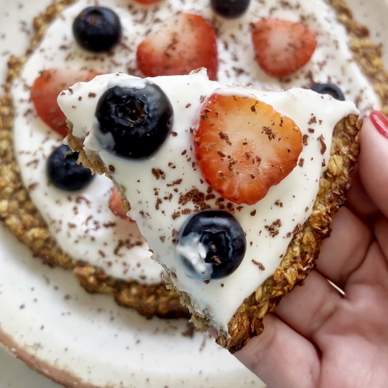 Healthy oatmeal breakfast pizza topped with yoghurt, strawberries, blueberries, and dark chocolate shavings.