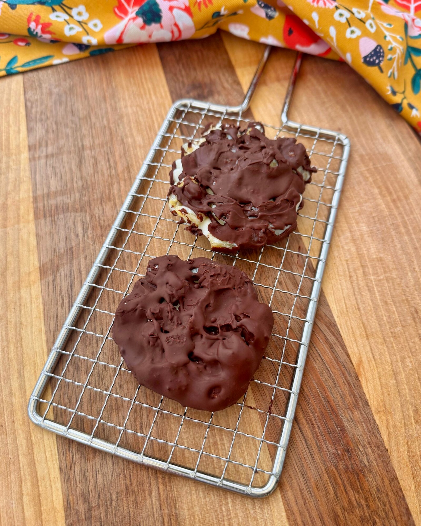 A close-up of four frozen pineapple and cottage cheese bites, coated in glossy dark chocolate, resting on parchment paper. The bites are round with visible pineapple chunks and sprinkled chia seeds, offering a contrast of textures and colors. Perfect as a healthy, high-protein snack or dessert.