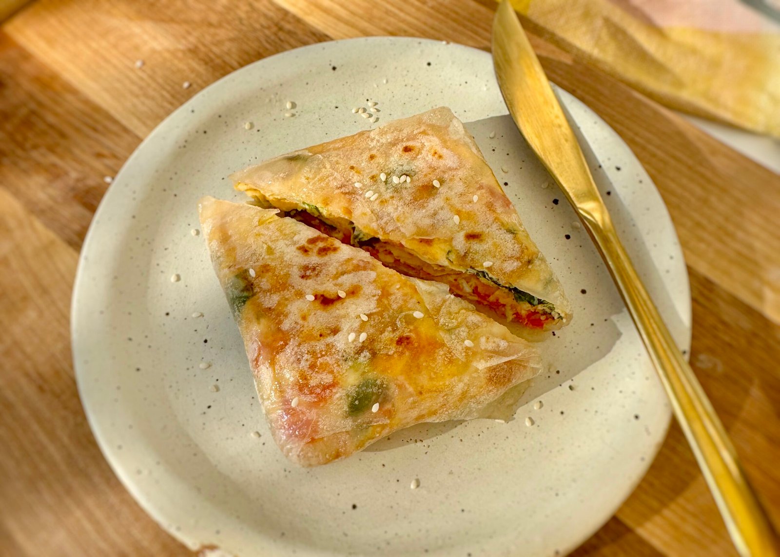 Golden brown rice paper omelette wrap sliced in half, filled with eggs, tomato, and spinach, garnished with sesame seeds.