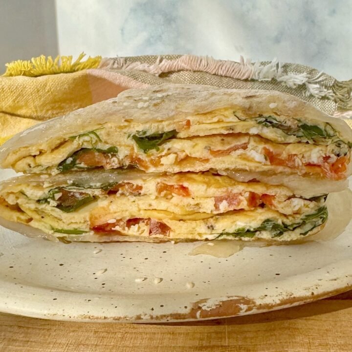 Golden brown rice paper omelette wrap sliced in half, filled with eggs, tomato, and spinach, garnished with sesame seeds.