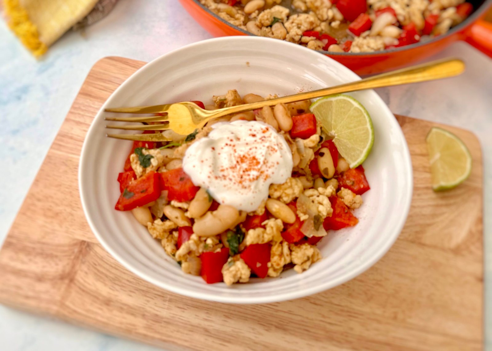 Bowl of turkey and white bean chilli topped with Greek yoghurt, chopped coriander, and a lime wedge, served in a rustic dish with tortilla chips on the side.