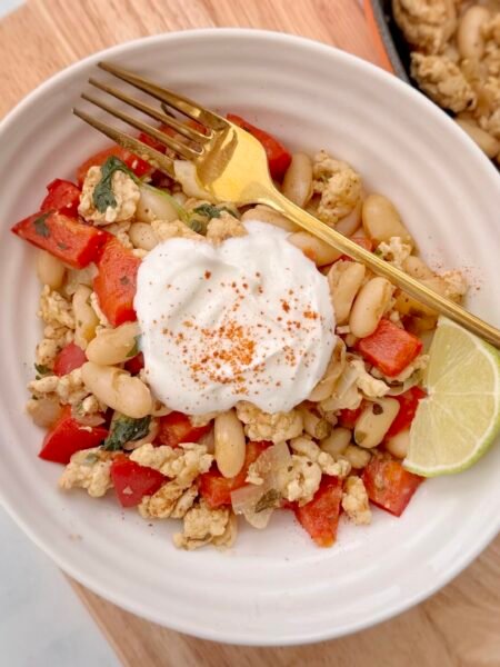 Bowl of turkey and white bean chilli topped with Greek yoghurt, chopped coriander, and a lime wedge, served in a rustic dish with tortilla chips on the side.