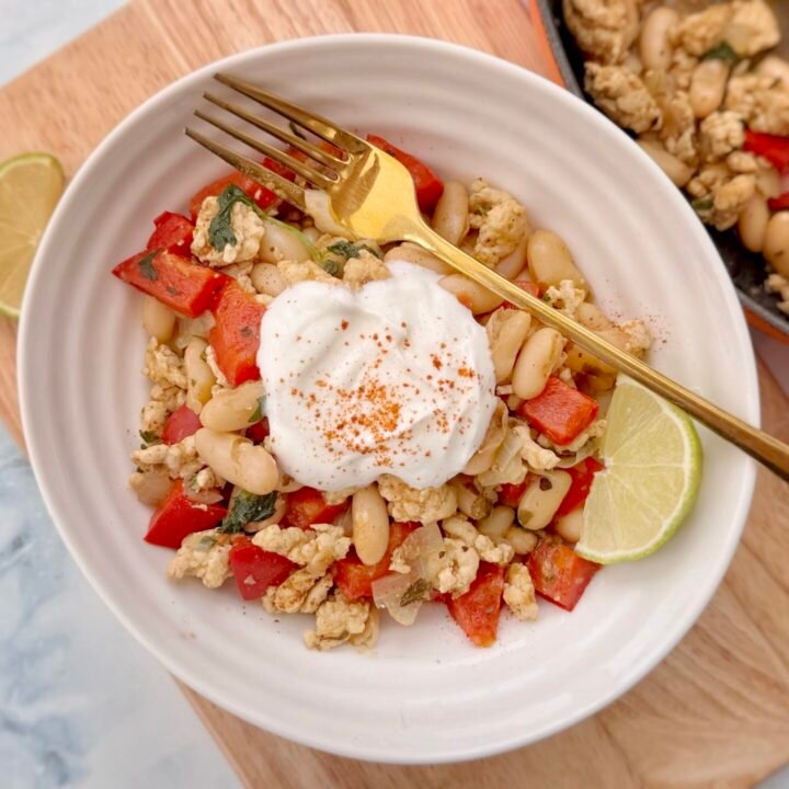 Bowl of turkey and white bean chilli topped with Greek yoghurt, chopped coriander, and a lime wedge, served in a rustic dish with tortilla chips on the side.