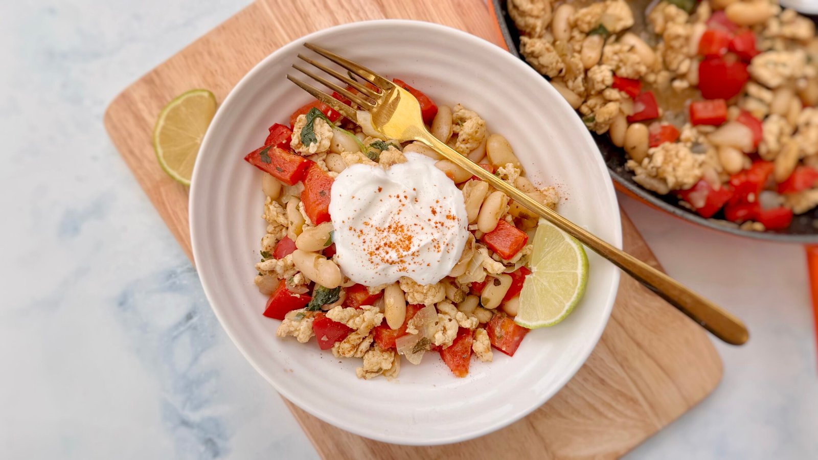 Bowl of turkey and white bean chilli topped with Greek yoghurt, chopped coriander, and a lime wedge, served in a rustic dish with tortilla chips on the side.